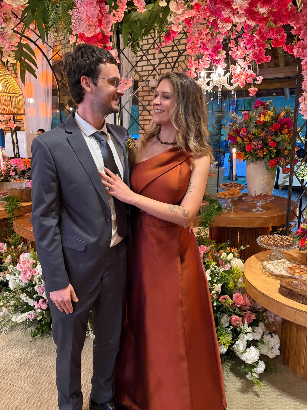 Rafaela e Lukas sorrindo em uma festa entre flores